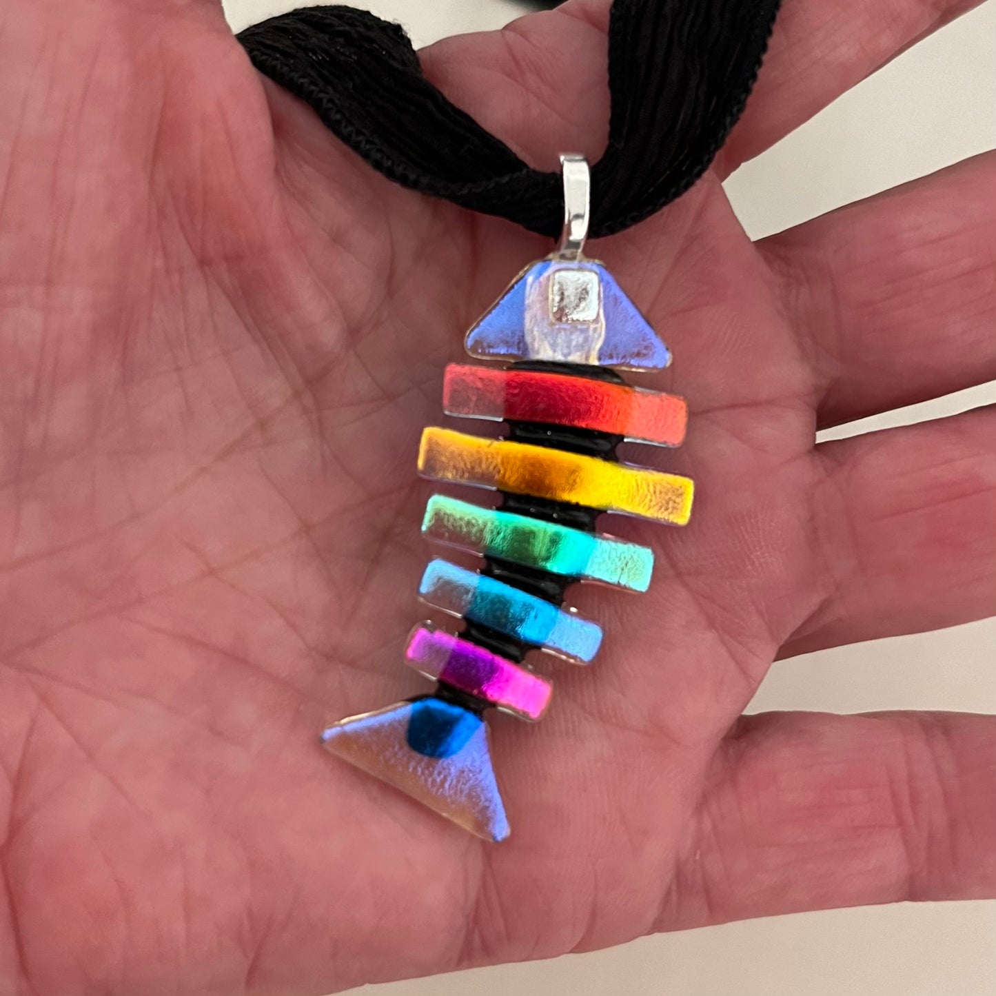 This is a favorite color combo! Large dichroic fused glass bonefish pendant with black spine, blue head & tail, multi-colored ribs, 2" in length, silver plated bail. * Chains & cords are not included but are available for purchase.